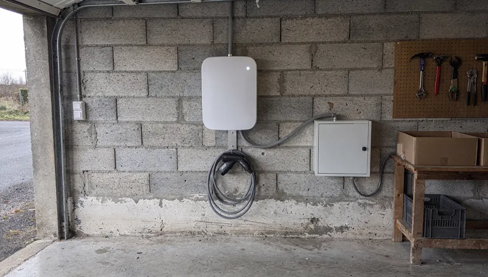 Borne de recharge murale dans un garage en parpaings, reliée à un coffret électrique