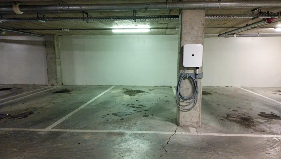 Borne de recharge murale fixée sur un pilier, à côté d'une place de parking souterrain
